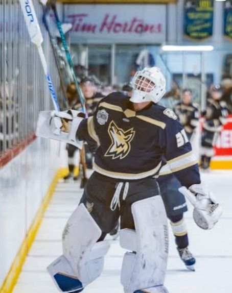 Osoyoos Coyotes goalie in navy and gold celebrating along the boards
