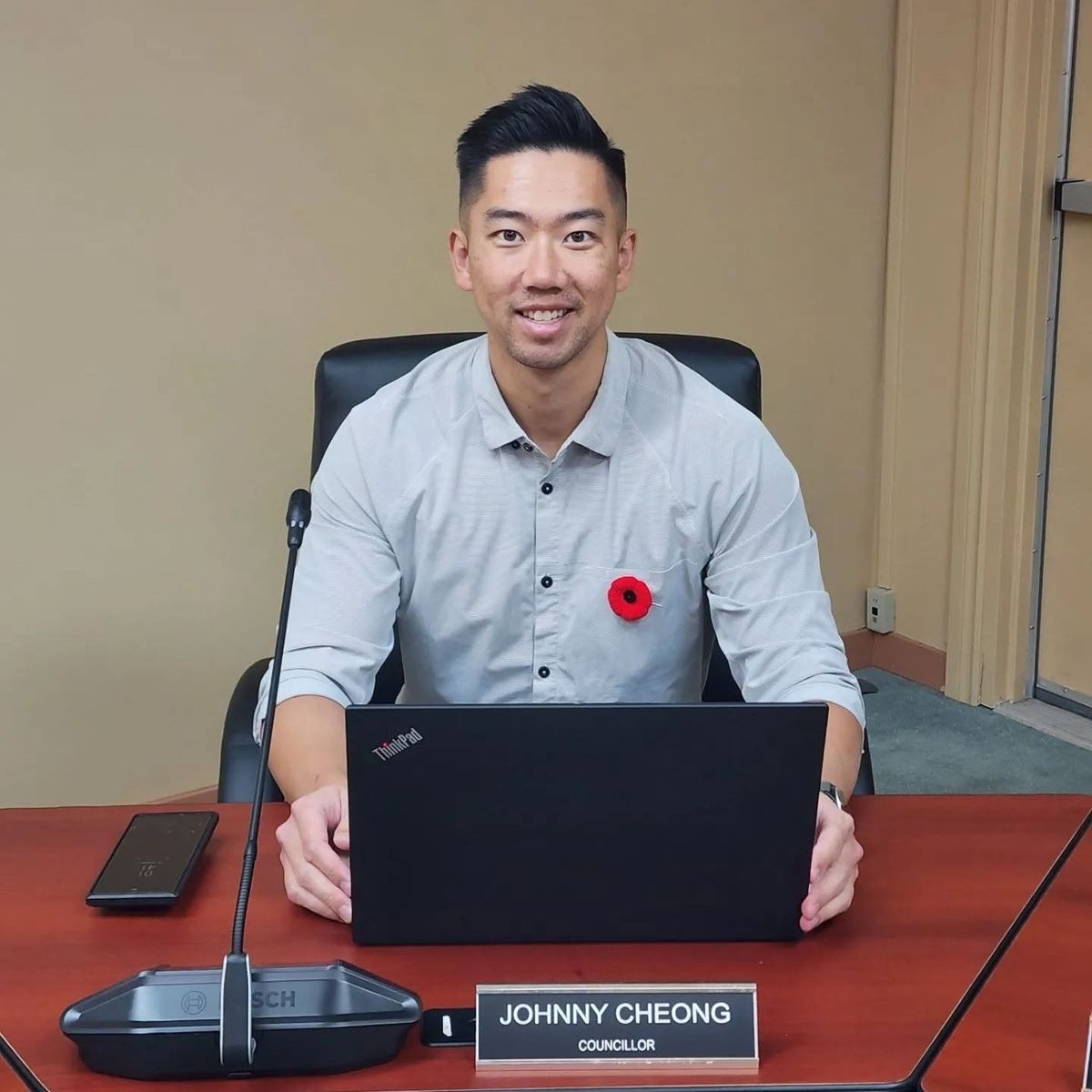 Johnny Cheong seated at the council table behind a nameplate reading Johnny Cheong, Councillor