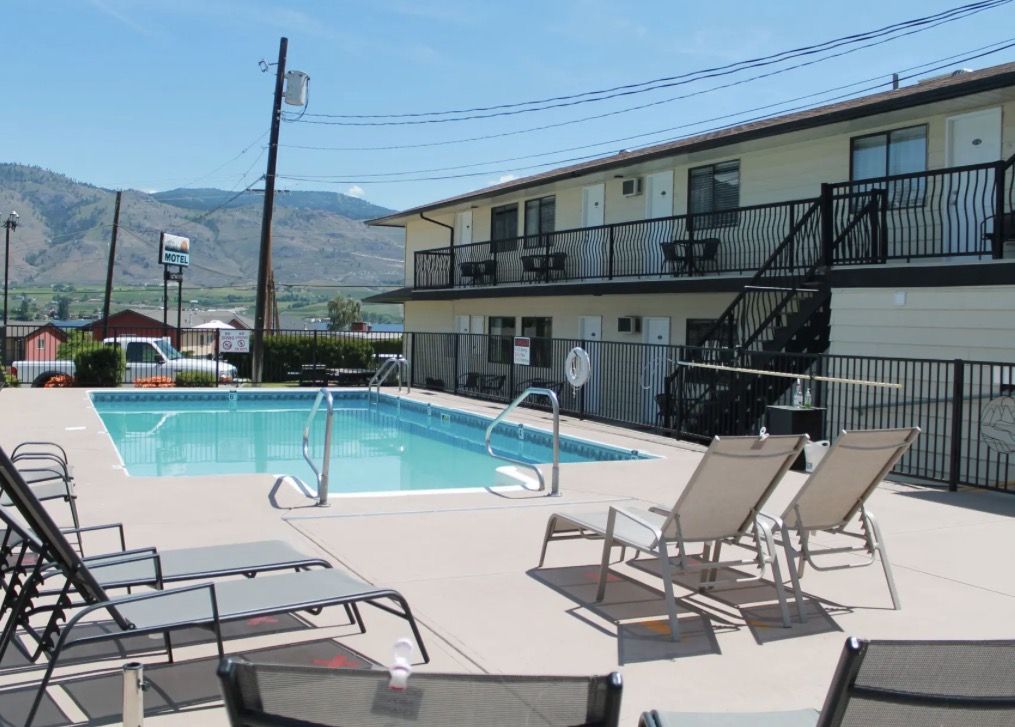 Outdoor pool and lounge chairs at a two-storey motel, with hills behind